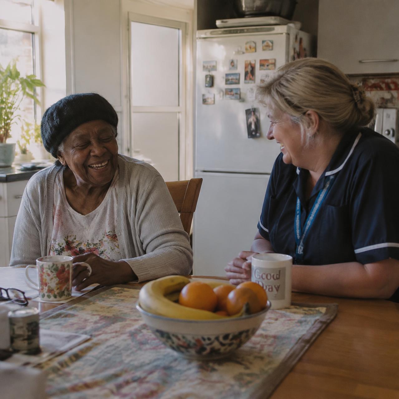 An older lady laughing with her Caronne Care carer at the kitchen table